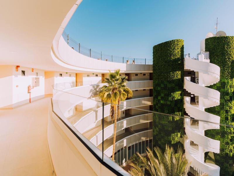 Uitzicht op een modern hotel met spiraaltrappen en met groen bedekte zuilen onder een blauwe lucht.