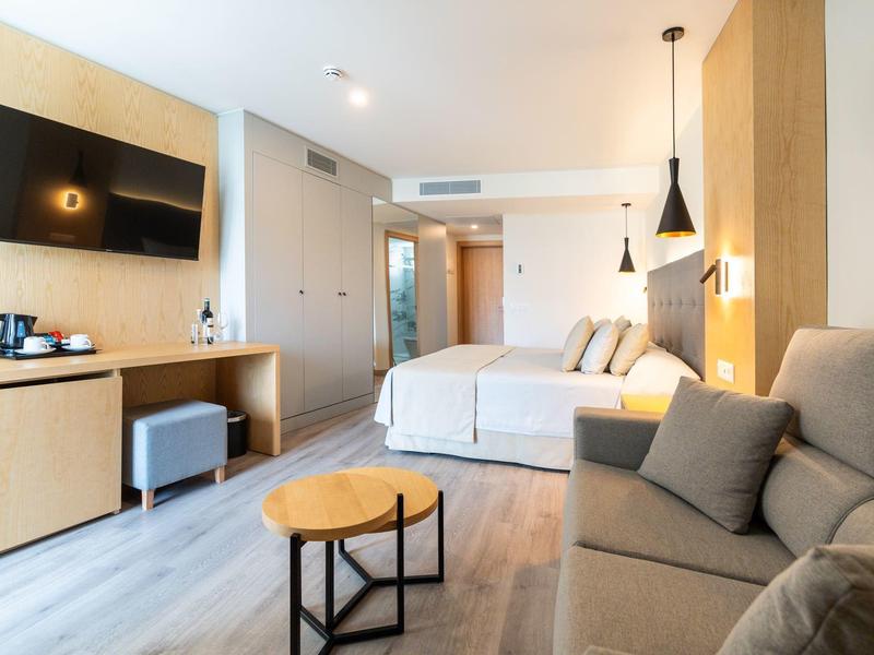 Modern hotelkamer met tweepersoonsbed, bank en aan de muur gemonteerde tv.