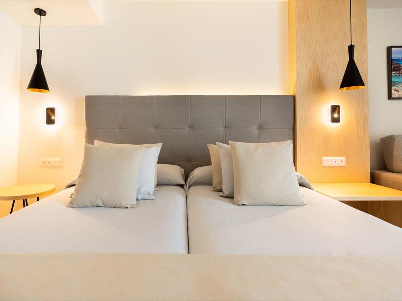 Moderne hotelkamer met twee eenpersoonsbedden, grijze hoofdbord en minimalistisch ontwerp.