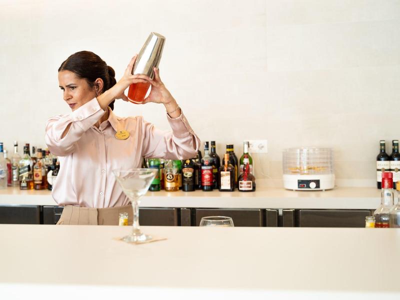 Een barman schudt een cocktailshaker achter een bar met verschillende flessen.
