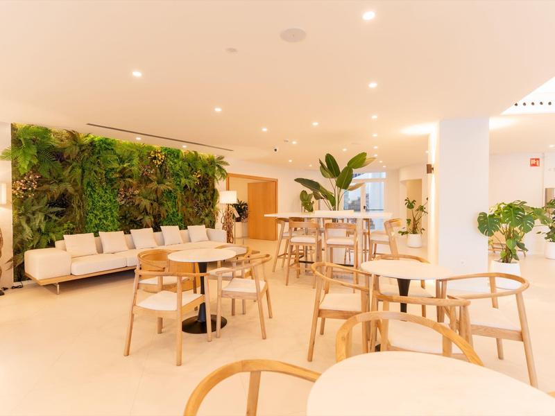 Lichte hotel-loungeruimte met houten stoelen, banken en groene planten aan de muur.