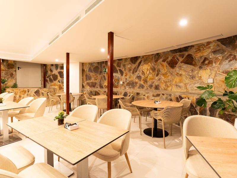 Licht hotelrestaurant met moderne houten tafels, comfortabele witte stoelen en decoratieve natuurstenen muur.