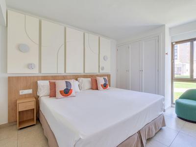 Modern hotel room with large bed, white bedding, and decorative pillows next to a window.