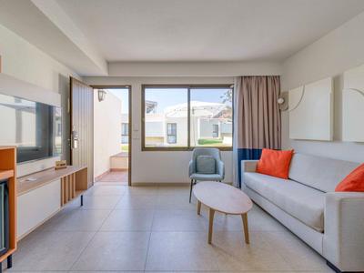 Modern hotel room with cozy sofa, armchair, TV, and balcony access.