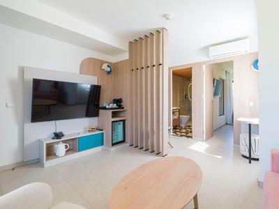 Bright hotel room with TV, modern furniture, and a round wooden table.