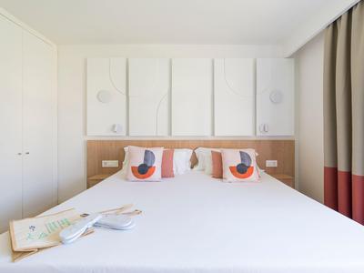 Modern hotel room with double bed, decorative pillows and light wood, minimalist design.