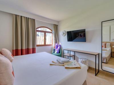 Modern hotel room with double bed, wall-mounted TV, and window with brown curtains.