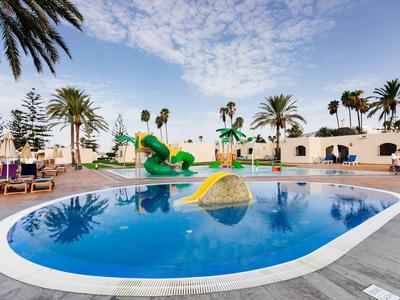 Outdoor pool with water slide and palm trees at a sunny vacation spot.