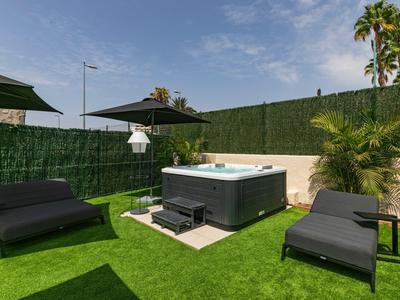 Modern outdoor area with hot tub, sun loungers, and sun umbrella on green lawn.