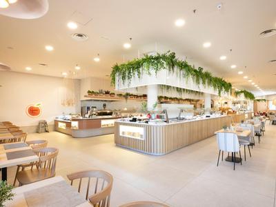 Spacious modern restaurant with bright interior and decorative plants above the buffet counter.