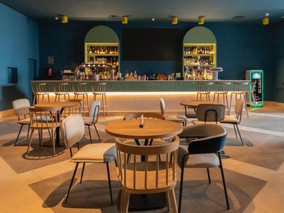 Modern hotel bar with wooden chairs, tables, and warm lighting in a blue room.