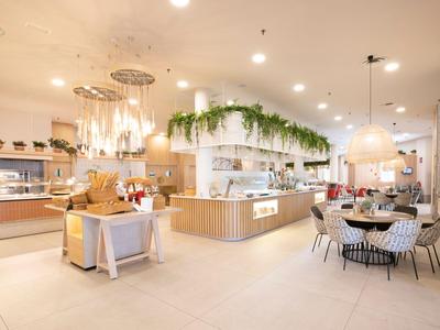 Bright, modern hotel restaurant with buffet area, set tables, and plants above buffet.