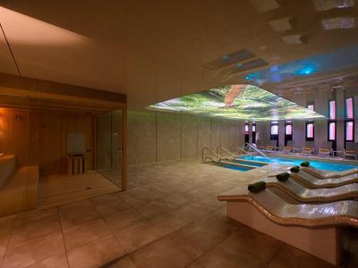 Modern hotel pool area with loungers, subdued lighting, and large windows.