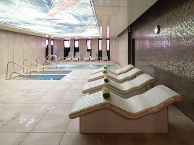 Modern indoor pool with loungers and artistic ceiling panel in a hotel.