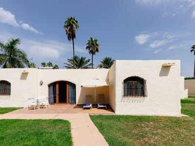 A beige hotel building with green lawn and palm trees around.