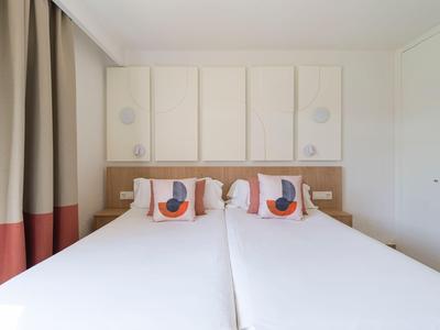 Modern hotel room with two single beds, decorative pillows, and minimalist wall decor.