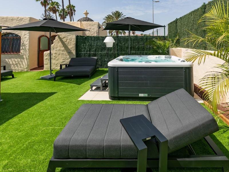 Modern hot tub on terrace with sun loungers and artificial grass in sunny setting.