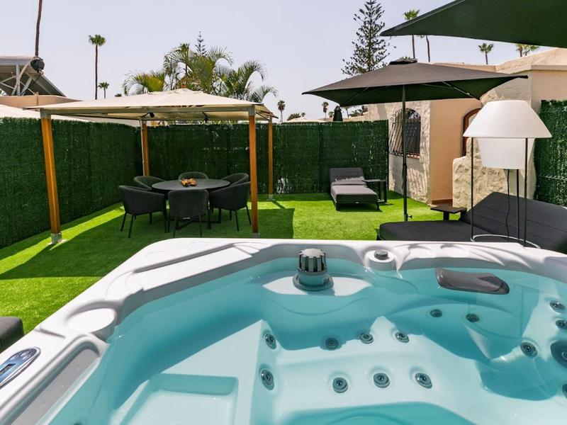 Modern hot tub on grass with umbrellas and garden furniture in the background.