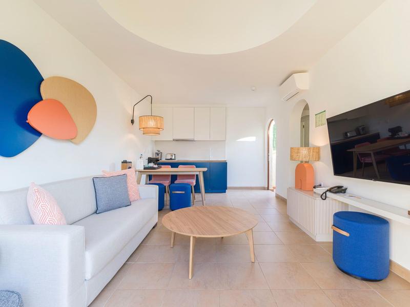Bright living area with white sofa, blue ottoman, and modern kitchen in the background.