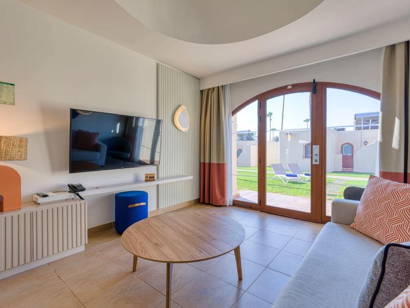 Bright living room with round window, sofa, coffee table, and garden view.