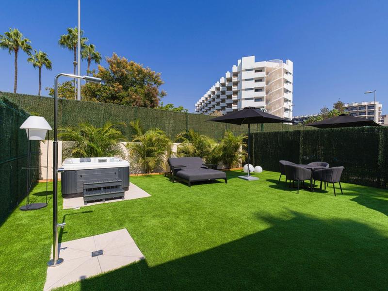 Modern garden area with lawn, lounge chairs, grill, and seating set in front of hotel building.