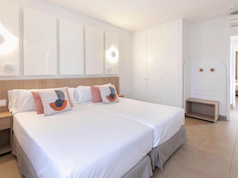 Modern hotel room with two single beds, decorative pillows, and minimalist design.