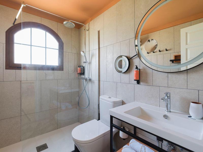 Modern bathroom with walk-in shower, toilet, and sink under a round mirror.