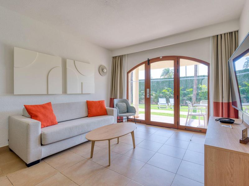 Living room with sofa, orange cushions, wooden coffee table, and large window to terrace.