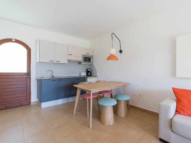 Modern kitchen area with wooden bench, colorful stools, and cozy sofa with orange pillow.