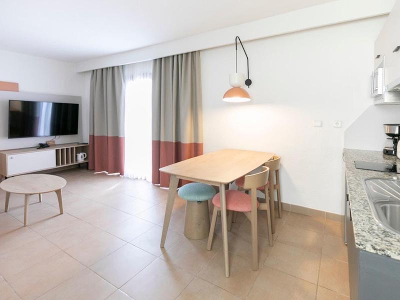 Modern dining area with table, chairs, kitchenette, and TV in a bright room.