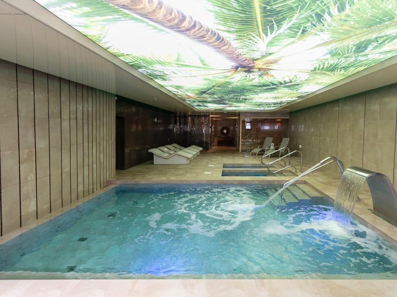 Modern indoor spa with hot tub, waterfall feature, and relaxing palm tree ceiling lighting.