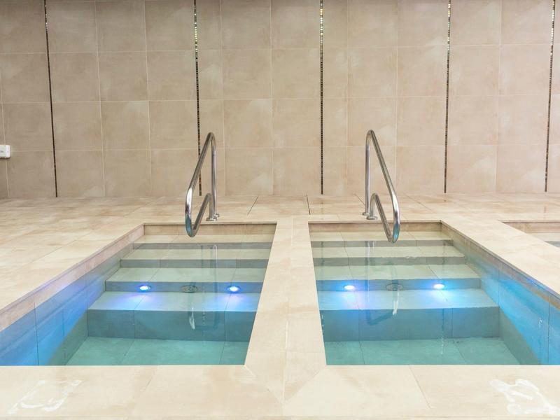 Two small heated pools with stairs and blue underwater lights in an indoor area.