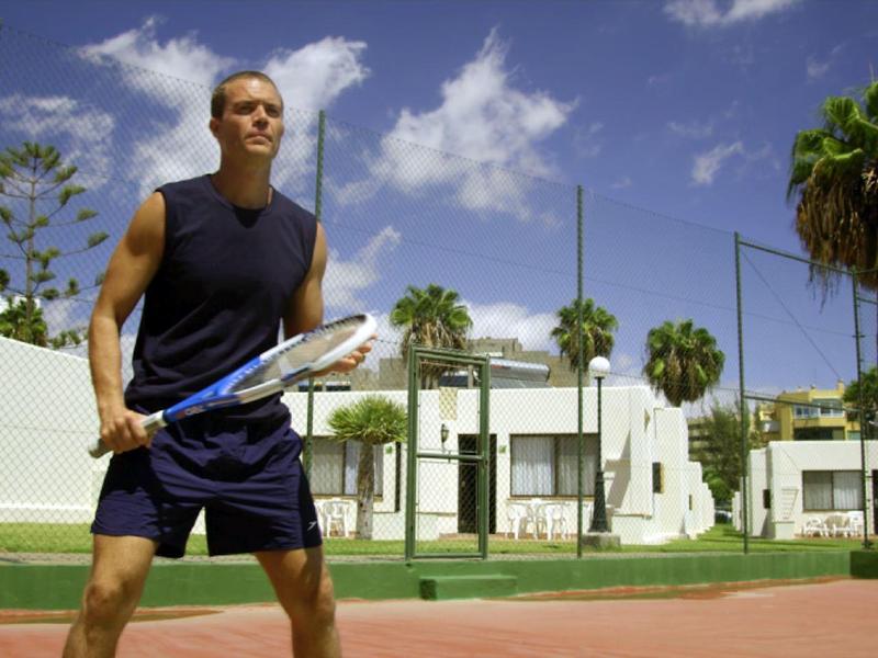 Man in sportswear holding tennis racket on sunny tennis court with palm trees.