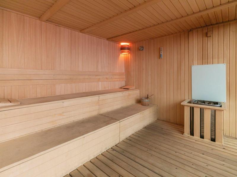 Wooden sauna with two seating levels and a heater on the wall.