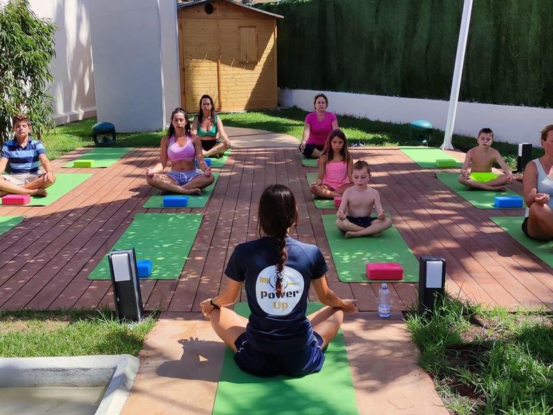 Group practicing yoga outdoors on mats next to a pool in a green setting.