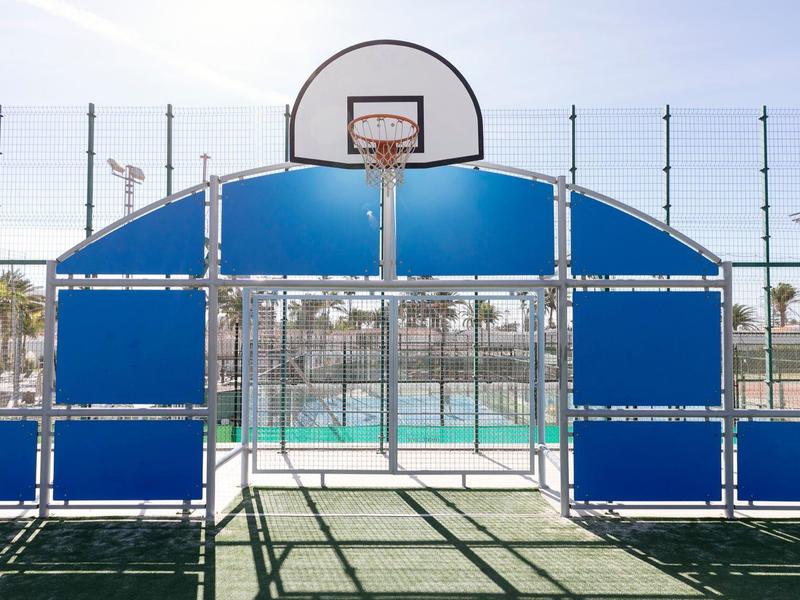 A basketball hoop surrounded by blue protective panels on a sunny outdoor court.