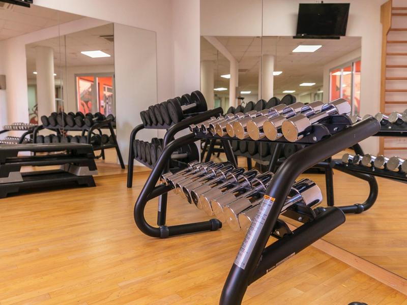Gym room with dumbbells, mirrors, wooden floor, and a wall-mounted TV.