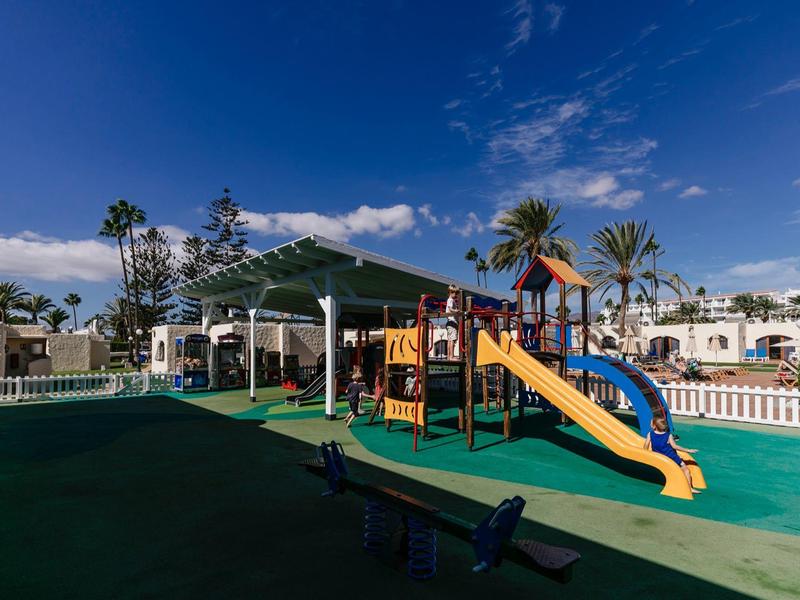 Children's playground with slide and climbing frame under blue sky in a holiday resort.