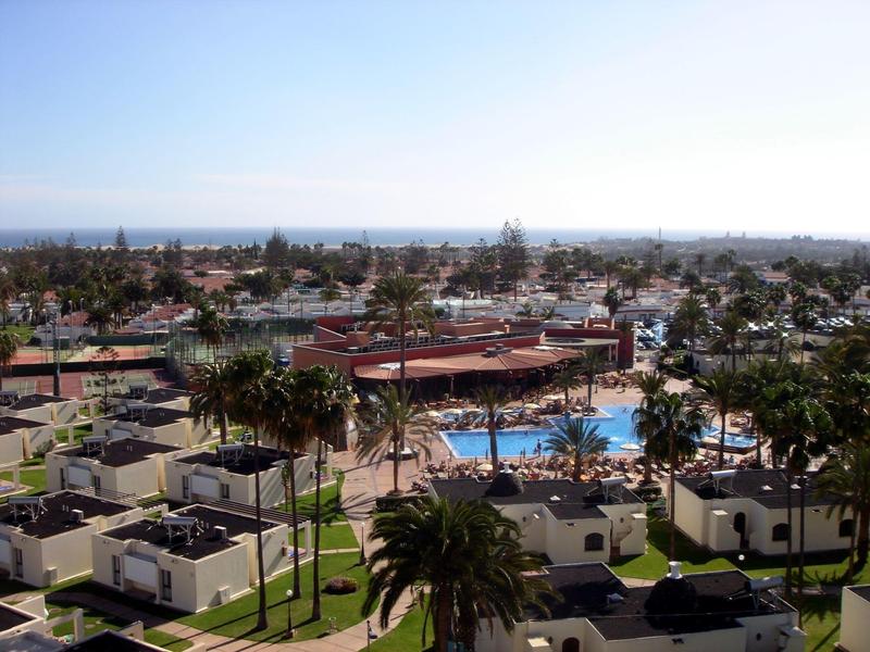 View of a hotel resort with pool, palm trees, and sea on the horizon under clear sky.