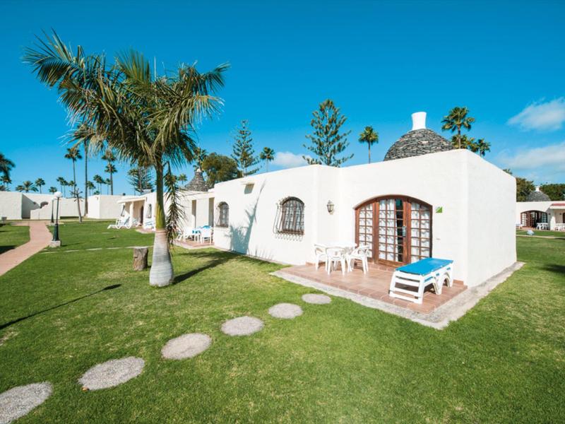 White holiday house with rounded roof, terrace, and palm trees in sunny weather.