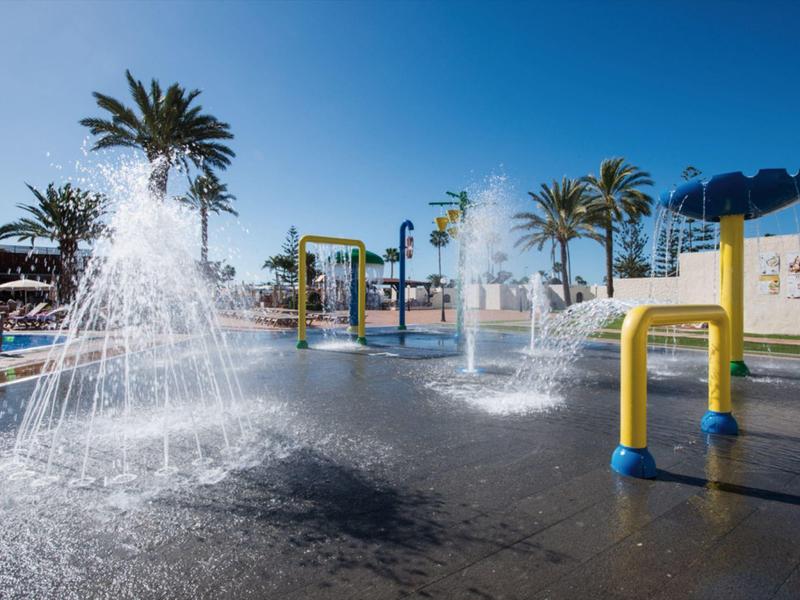 Water playground with fountains and palm trees under a clear blue sky at a resort.
