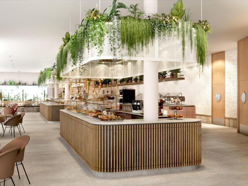 Modern hotel restaurant with wooden buffet, plant decor, and comfortable seating.