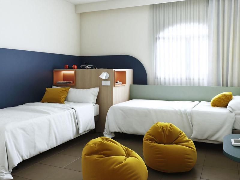Bright hotel room with two single beds, bean bag chairs, and large window with curtains.