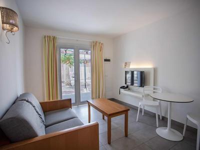 Bright, simple living room with sofa, wooden table, small white table, and window to the terrace.