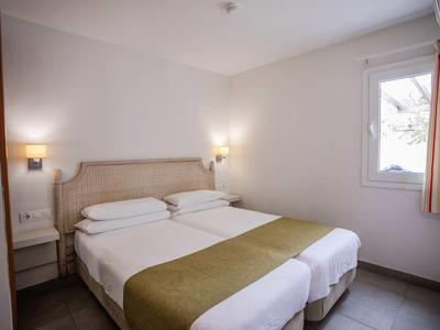 Simple hotel room with two single beds, bedside table, and window with curtains.