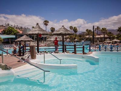 Groot hotelzwembad met zonneschermen en blauw water onder heldere lucht