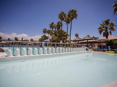 Zwembad met witte decoratieve elementen, palmbomen en zonneterras op de achtergrond onder een heldere lucht