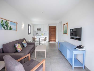 Modern living room with sofa, kitchenette, and TV in bright colors.