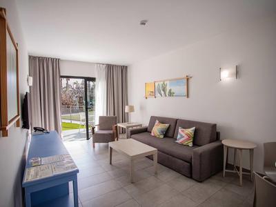 Bright living room with sofa, coffee table, chairs, and garden access in daylight.