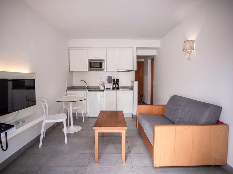 Modern living room with gray sofa, small wooden table, white chairs, and kitchen area.